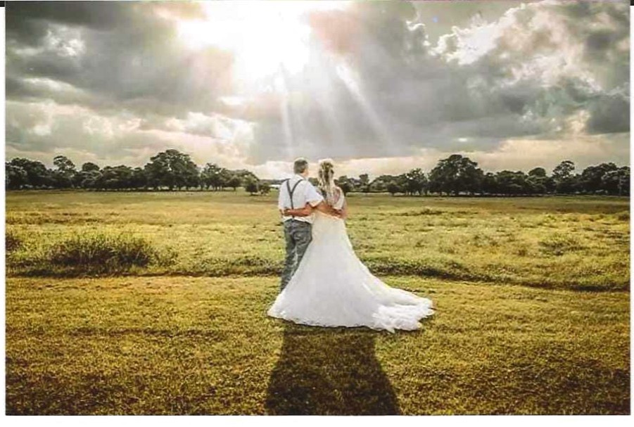 A bride and groom embracing in a vast, sunlit golden field under a dramatic Missouri sky at our country wedding venue.