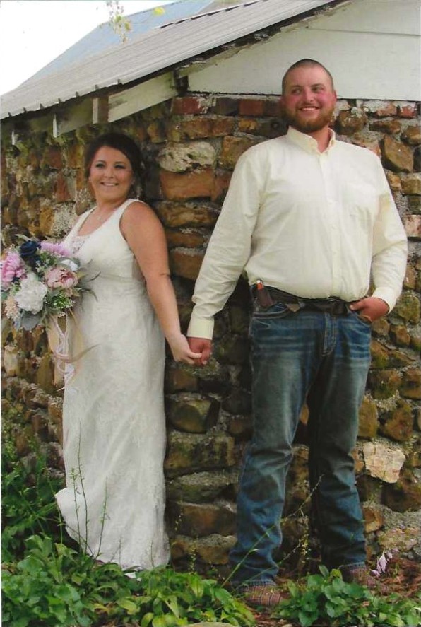 A bride and groom holding hands and smiling while posing against a rustic textured stone wall at our country wedding venue.