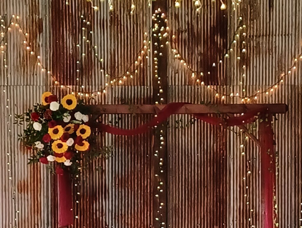 Close up of a rustic wedding arch floral arrangement with sunflowers and burgundy roses