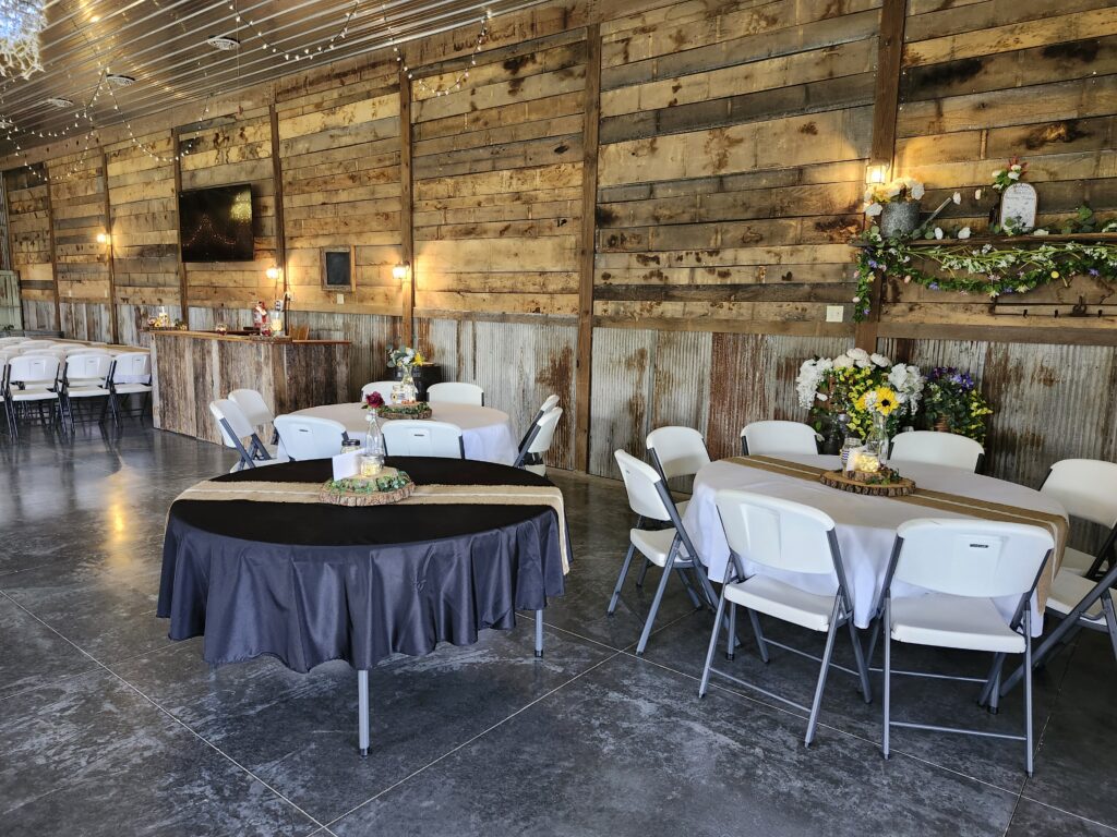 An indoor wedding reception hall setup with a round table in a black tablecloth and a round table decorated with sunflowers and burlap runners.