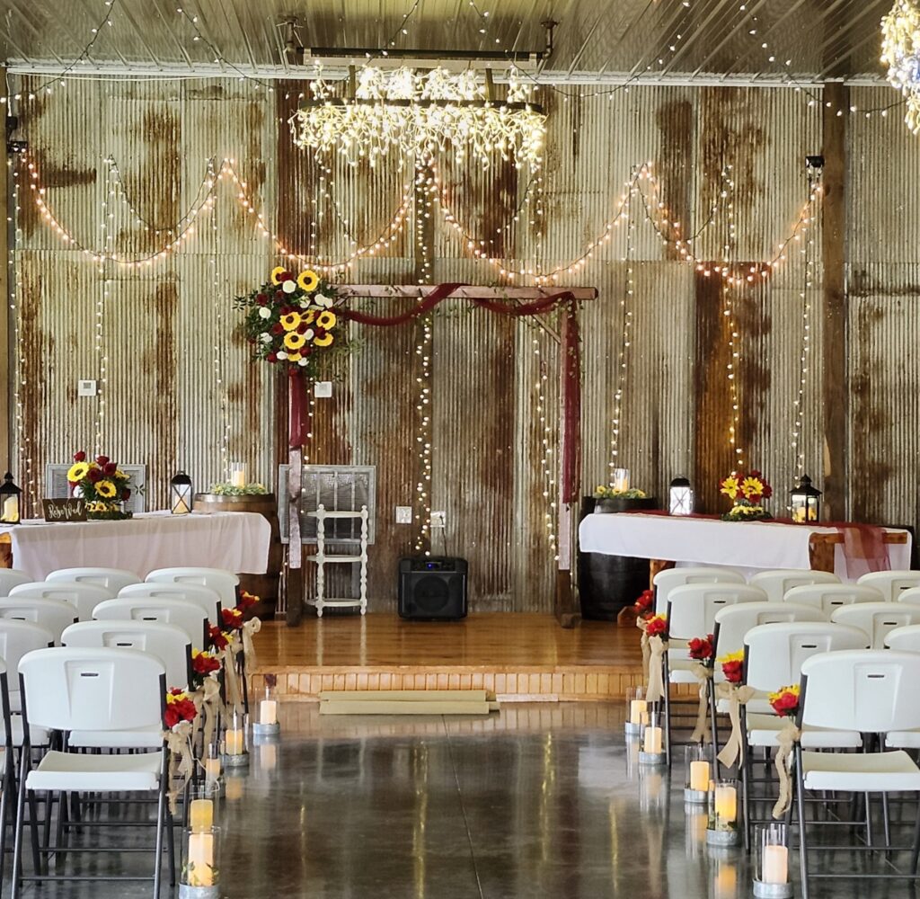 Vibrant sunflower and red rose floral arrangements decorate an indoor rustic wedding ceremony space at Country Charm Venue