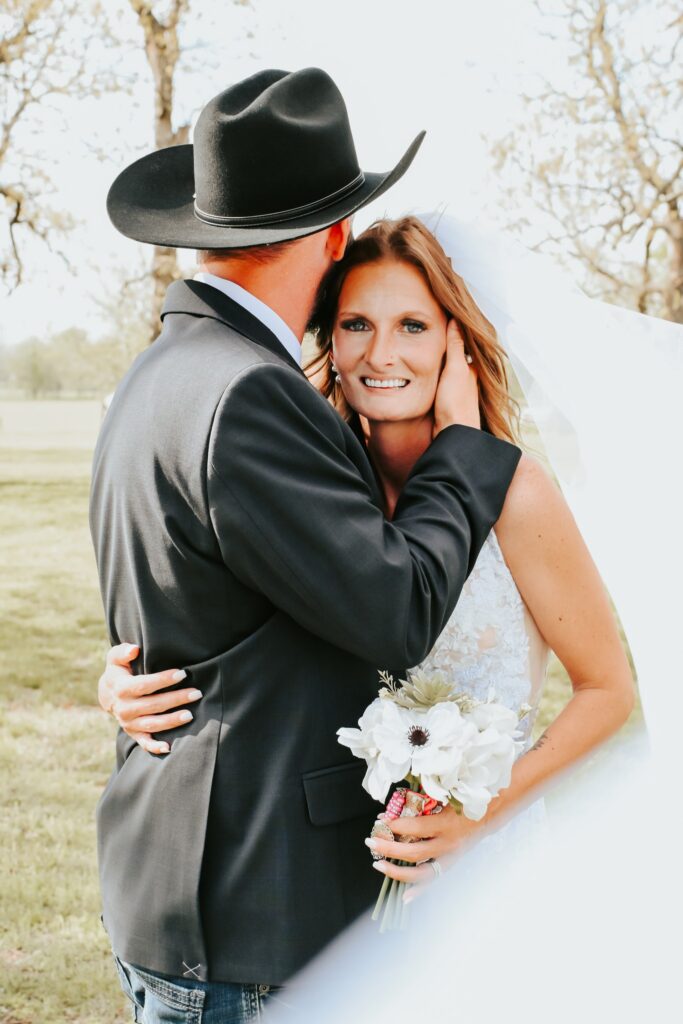 Bride in lace wedding dress and groom in black cowboy hat at an outdoor country wedding