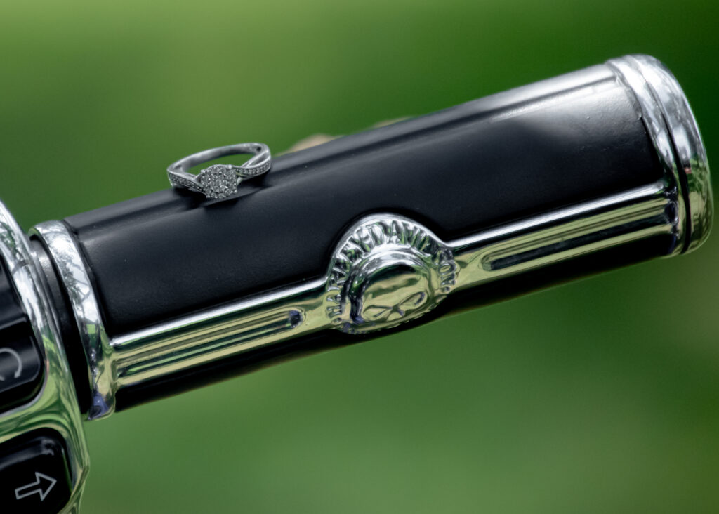 A closeup of an engagement ring on the handlebar of a motorcycle.