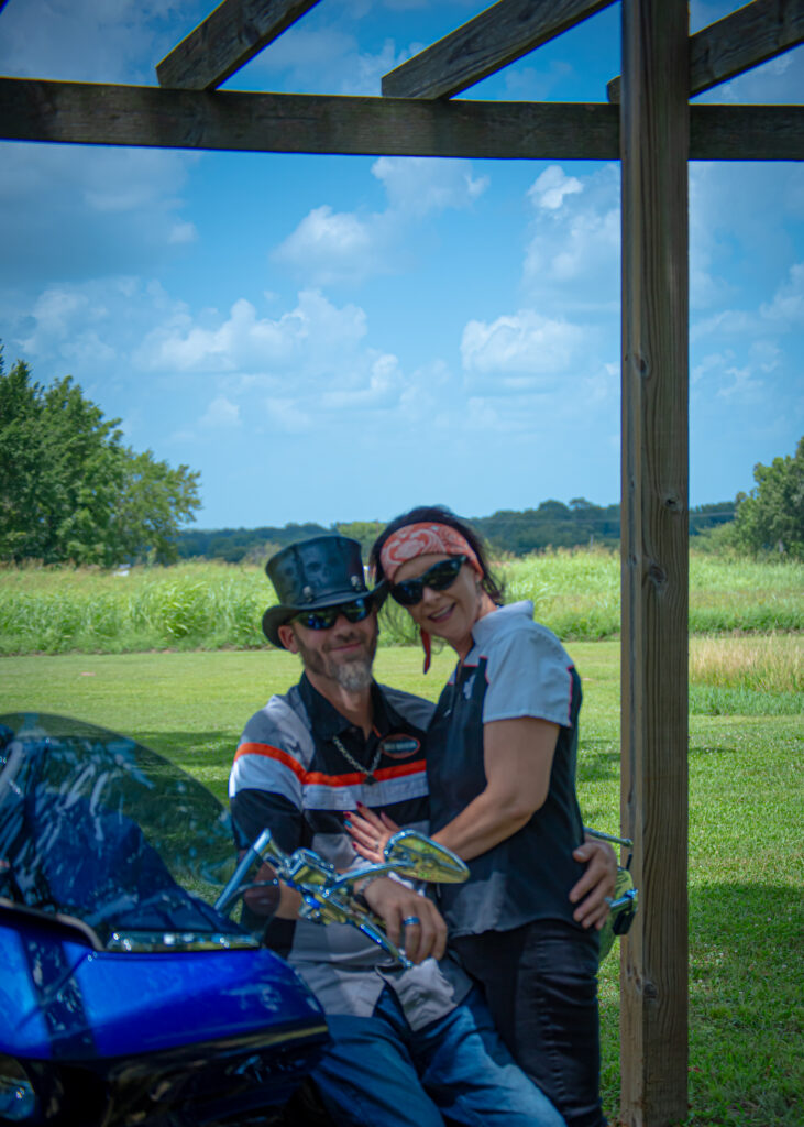 Couple on Harley Davidson motorcycle framing the handcrafted wooden arbor at Country Charm Event Venue